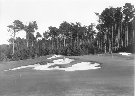 Dr. Alister MacKenzie hitting out of a bunker on the 2nd hole with Hilda holding the pin and her friend on the green 1930